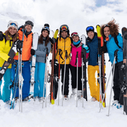 Grup d’amics somrient a la neu amb els esquís i els bastons
